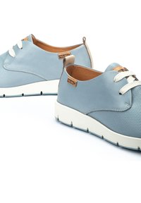 Zapatillas de cuero azul claro con un diseño perforado, cordones blancos y detalles en marrón, con una suela blanca gruesa. Marca Pikolinos visible.