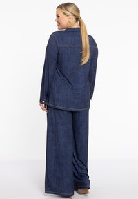 Denim twee-delige outfit bestaande uit een shirt met lange mouwen en een kraag, en wijde broekspijpen, beiden in een donkerblauwe tint met contrasterende stiksels.
