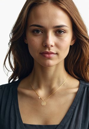 Goldene Halskette mit einem runden Anhänger im Gitterdesign und einem kleinen Perlenakzent, getragen über einem dunklen, strukturierten Oberteil.
