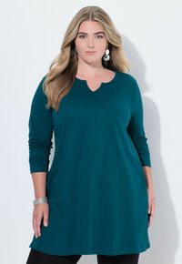 Türkisfarbene Langarm-Tunika mit V-Ausschnitt und lässiger Passform. Glatter, dehnbarer Stoff in einfarbiger Ausführung, kombiniert mit schwarzen Leggings.