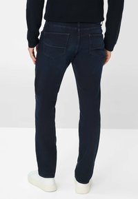 Jeans blu navy con una vestibilità slim, realizzati in denim. Presentano due tasche posteriori e una finitura leggermente teksturata, indossati con sneakers bianche.
