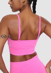 Różowy dopasowany crop top z cienkimi regulowanymi ramiączkami, wykonany z elastycznego materiału, o gładkiej fakturze i minimalistycznym wzornictwie.