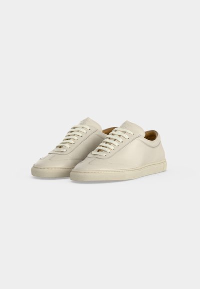 Ζευγάρι μπεζ χαμηλά sneakers με κορδόνια και λεία δερμάτινη υφή σε απλό ανοιχτό φόντο.