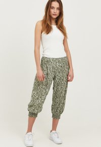 Lettere, grønne blomster-mønstrede joggerbukser med elastiske manchetter, parret med en hvid tanktop og hvide sneakers.