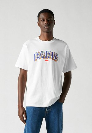 Valkoinen puuvillapaita, jossa on värikäs "PARIS" -grafiikka edessä. Suora leikkaus, lyhyet hihat ja pyöreä pääntie.
