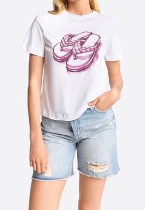 White short-sleeve shirt with a pink sketch of braided sandals, worn with light blue ripped denim shorts.