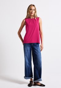 Top senza maniche fucsia con scollo arricciato, abbinato a jeans in denim a gamba larga e ballerine nere intrecciate, che mostrano un look casual per la giornata.