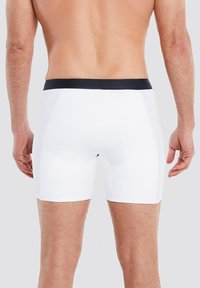 Weiße Boxer-Briefs mit einem marineblauen Taillenbund, die eine enge Passform und eine glatte Textur aufweisen, mit einer nahtlosen Rückseite und Oberschenkel-Länge.