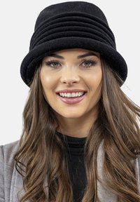 Cappello a secchiello nero realizzato in tessuto morbido, con pieghe orizzontali attorno alla corona e un ampio bordo arrotondato. Nessun logo o accentuazione visibile.