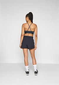 Svart sportbh med korslagda ryggband, kombinerad med matchande svarta shorts. Plaggen är tillverkade av ett glatt, andningsbart material.