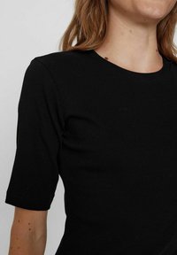 Top noir à manches courtes en ribbed avec un col rond, présentant un design ajusté et une texture lisse, idéal pour une tenue décontractée.