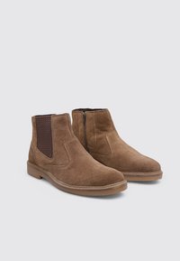 Braune Wildleder-Stiefeletten mit elastischen Seitenpaneelen und einem strukturierten Akzent. Sie verfügen über eine niedrige Gummisohle und ein glattes, rundes Zehendesign.