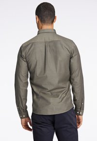 Camisa de manga larga en tela verde oliva, con un cuello abotonado, textura sutil y detalles de botones en las mangas.