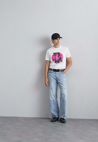 Weißes T-Shirt mit grafischem, pinkfarbenem Kreis, kombiniert mit hellblauen Jeans mit auffälligen Nahtakzenten und schwarzen Schuhen.