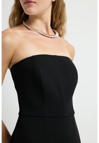 Vestido negro sin mangas con corsé estructurado y costuras verticales. Collar de metal plateado con un diseño suave y curvado alrededor del cuello.