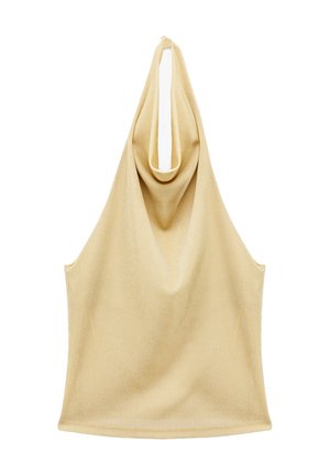 Giovane donna che indossa un top beige senza maniche a collo alto, jeans larghi scuri, scarpe nere con punta e orecchini a cerchio dorati, in piedi su sfondo bianco.