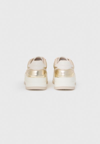 Beige sneakers med en teksturert overdel og metalliske gulldetaljer. Synlig logo på hælen. Tykk hvit gummisåle for ekstra høyde.