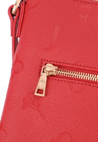 Borsa a tracolla in pelle rossa con texture e motivi in rilievo. Presenta una cerniera dorata con un tirante a logo e cuciture dettagliate.