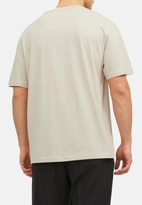 Kurzärmliges T-Shirt mit Rundhalsausschnitt aus leichtem beigen Baumwollstoff. Es hat eine lockere Passform, eine glatte Textur und einen geraden Saum an der Unterseite.