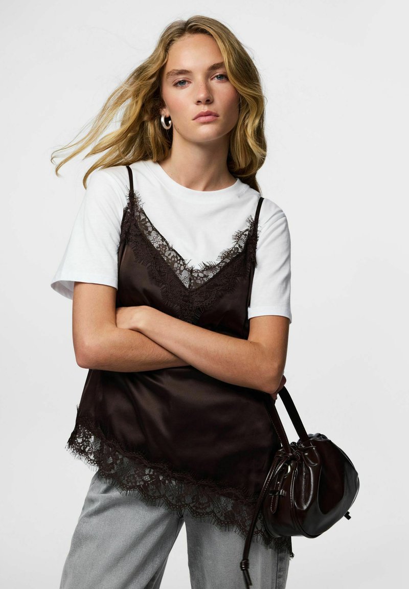 Sort sateng camisole med blonder over en hvit t-skjorte, kombinert med lysegrå jeans og en liten svart håndveske. Modell med langt, bølgete hår.