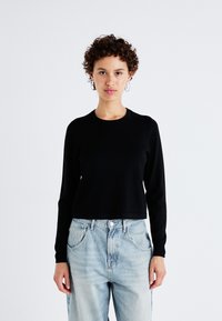 Zwarte lange mouw cropped trui met een ronde hals, gemaakt van een gladde stof. Gecombineerd met lichtblauwe, los zittende denim jeans.