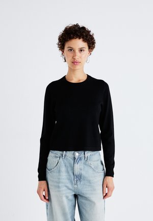 Zwarte lange mouw cropped trui met een ronde hals, gemaakt van een gladde stof. Gecombineerd met lichtblauwe, los zittende denim jeans.