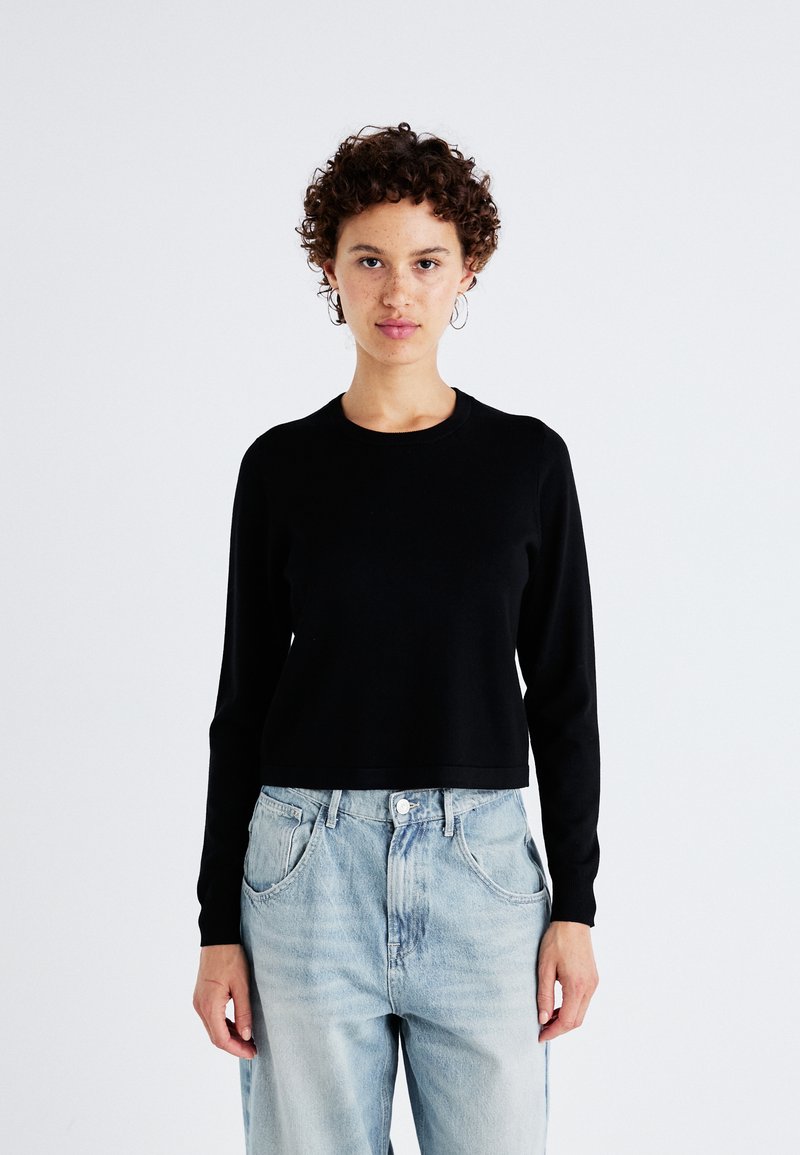 Zwarte lange mouw cropped trui met een ronde hals, gemaakt van een gladde stof. Gecombineerd met lichtblauwe, los zittende denim jeans.