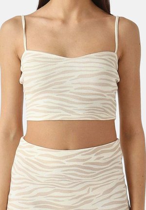 Vrouw draagt beige-wit zebraprint crop top met dunne bandjes en bijpassende high-waisted rok, torso zichtbaar van nek tot heupen.