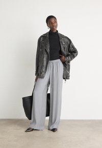 Svart skinnkjolejakke, svart turtleneck, løse grå vidde bukser, spisse svarte leiligheter og en stor svart tote-bag.