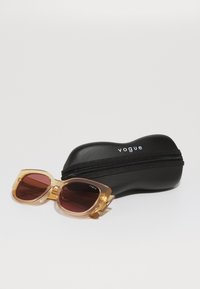 Ochelari de soare cu rame transparente de culoare chihlimbar și lentile întunecate, lângă un toc rigid negru, având inscripția "vogue" în text alb și un fermoar.