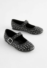 Chaussures Mary Jane en cuir noir avec des clous argentés, bout rond, talon plat et une sangle de verrouillage sur le côté pour un maintien sécurisé.