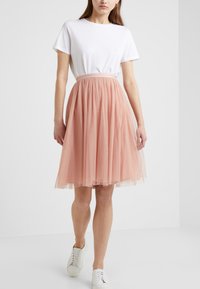 Gonna di tulle rosa chiaro con pois, vita elasticizzata, abbinata a una t-shirt bianca a girocollo e sneakers bianche.