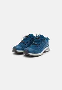 Chaussures de trail running en mesh bleu avec semelles en caoutchouc grises, dotées d'un col rembourré, de lacets élastiques et d'un design texturé et soutenant.