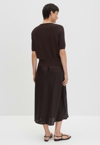 Haut marron foncé à manches courtes associé à une jupe longue fluide assortie, avec une texture lisse et une coupe décontractée. Des sandales simples complètent le look.