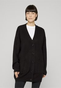 Črni pleteni kardigan z V-izrezom, dolgimi rokavi, gumbi spredaj in dvema stranskima žepoma. Iz mehkega, teksturiranega platna.