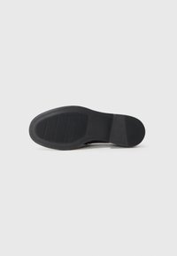 Semelle en caoutchouc noir avec surface texturée, présentant des lignes horizontales pour l'adhérence. Talon arrondi et design à bords lisses. Apparence simple et uniforme.