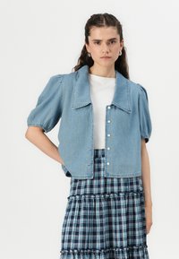 Lys blå denim kort jakke med stor krage, puffede ærmer og knaplukning, kombinert med et navy rutet lagdelt skjørt.