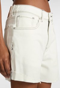 Shorts en denim blanc avec un ourlet effiloché, un design classique à cinq poches et des coutures contrastées. Le matériau présente une finition douce et texturée.