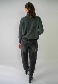 Pull gris avec col montant, associé à un jean droit noir légèrement délavé. Modèle portant des bottes à talon haut noires.