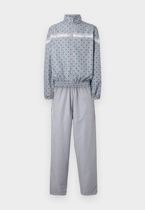 Lichtgrijze trainingsoutfit bestaande uit een ritsjack met geometrisch patroon en bijpassende broek, met elastische mouwen en tailleband.