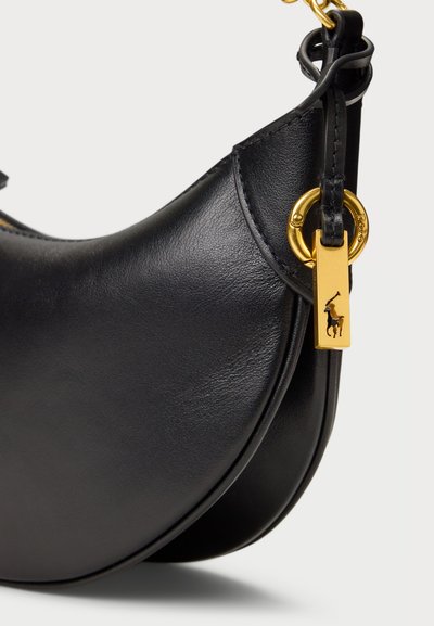 Črna usnjena torbica s ukrivljenim dizajnom, z zlatimi dodatki in oznako s logotipom. Gladka tekstura in minimalni poudarki.
