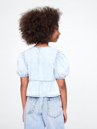 Lyseblå denim peplum-top med puffermer og knappelukking bak. Kombinert med lyseblå høytlivsjeans.