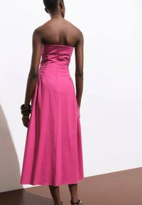 Abito rosa senza spalline con un corsetto aderente, dettagli arricciati e una gonna svasata. Tessuto dalla texture liscia, stile lungo fino al ginocchio.