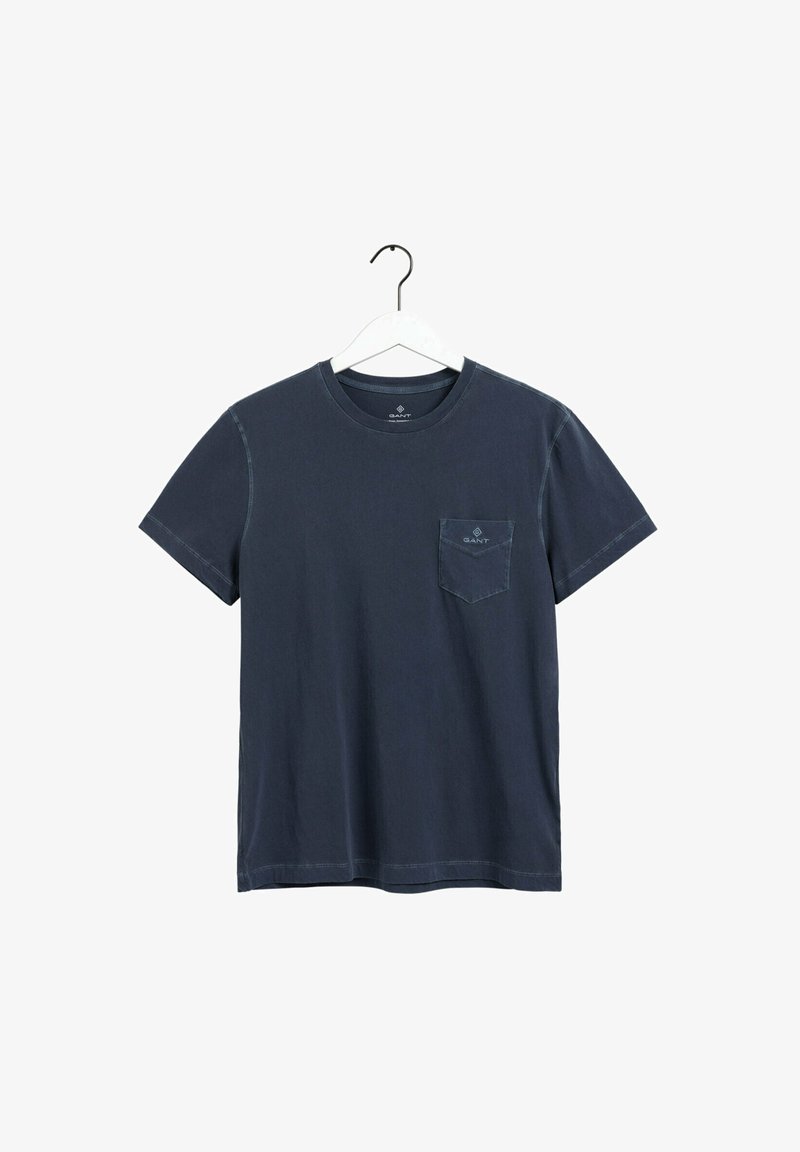 T-shirt bleu marine à manches courtes avec col rond et logo sur la poche poitrine, suspendu à un cintre blanc sur un fond blanc.
