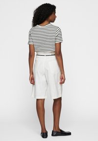 Pantalones cortos de lino blancos combinados con una camiseta recortada a rayas blancas y negras. El conjunto incluye un cinturón negro con un acento de logo.