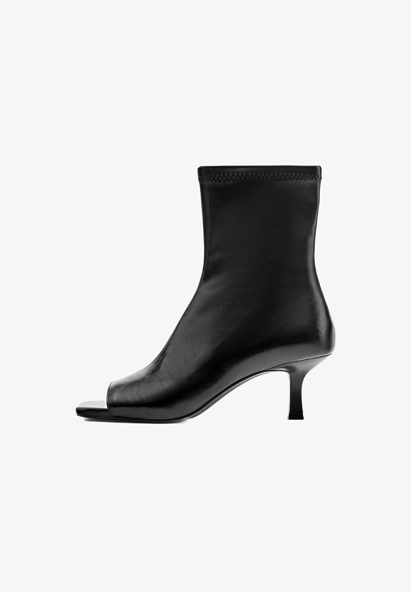 Bottine en cuir noir avec bout ouvert et petit talon, vue de profil sur fond blanc.