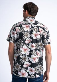 Camisa de manga corta hecha de una tela ligera que presenta un fondo negro con grandes patrones florales en blanco y rosa, y acentos en verde.