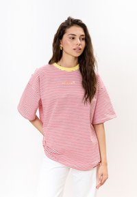 Rood-wit gestreept T-shirt met korte mouwen, gele halslijn en kleine geborduurde details aan de voorkant. Casual pasvorm en zachte stof.
