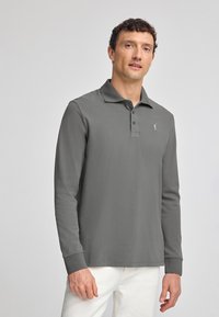 Grå långärmad polo tröja i strukturerad tyg, med krage, tre knappar och en liten logotyp på bröstet.