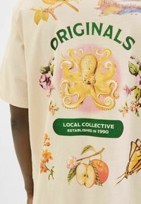 Beige színű pamut póló, élénk színű polip grafikával, virágos mintákkal és felirattal: "ORIGINALS" és "HELYI KOLLEKTÍV 1990-BEN ALAPÍTVA."